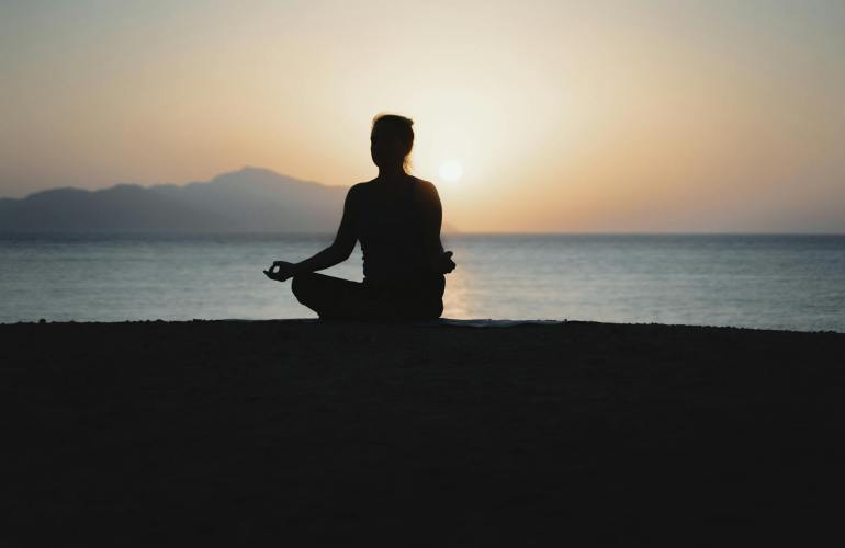 silhouette of a woman meditating by the ocean at sunset